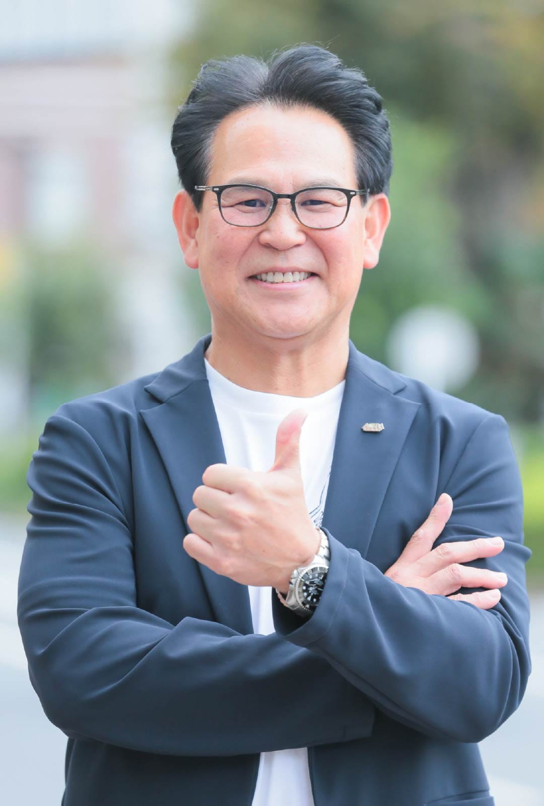 尾林代表が親指を立て、明るい表情でこちらに向かって微笑んでいる