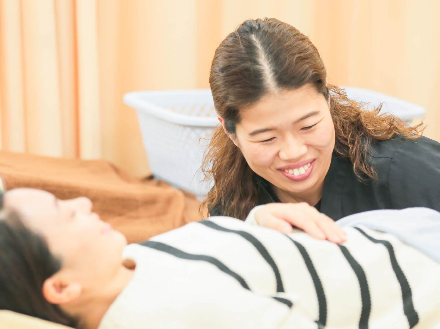 黒いユニフォームの女性スタッフが、施術台の患者様に笑顔で話しかけている様子
