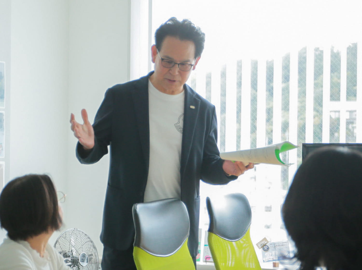 代表取締役社長 尾林 功二が、左手に冊子をもち従業員にレクチャーをしている様子