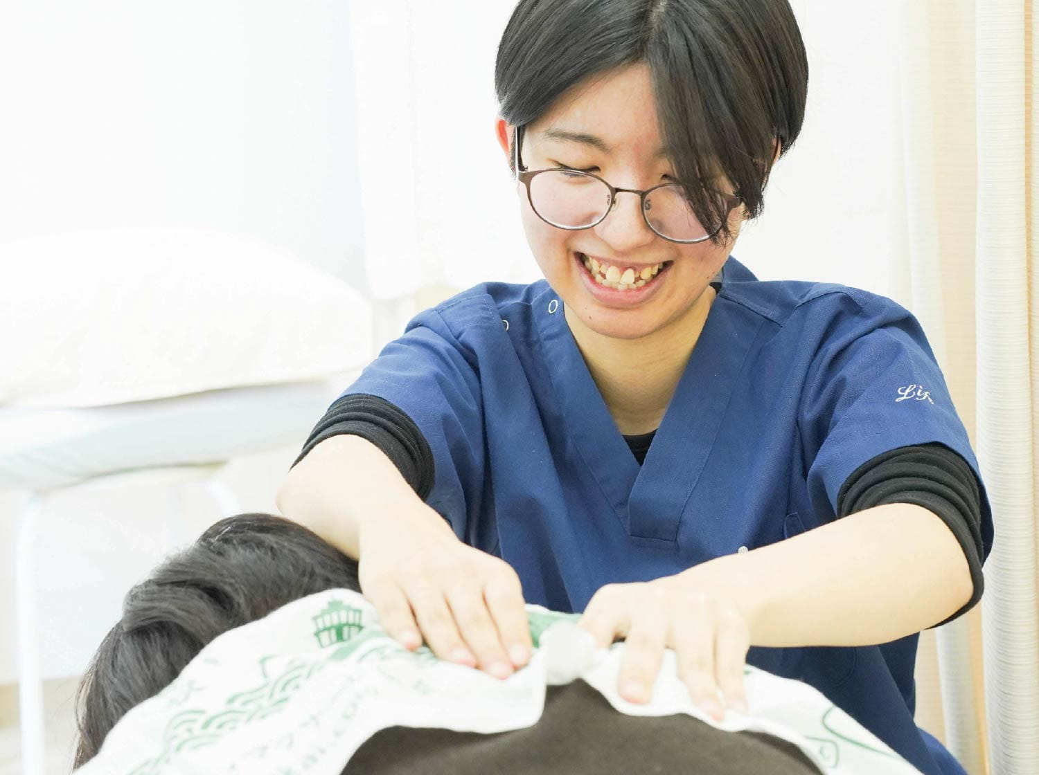 眼鏡の女性スタッフが、寝台に伏すお客様の頭部周りに手を添え施術している様子