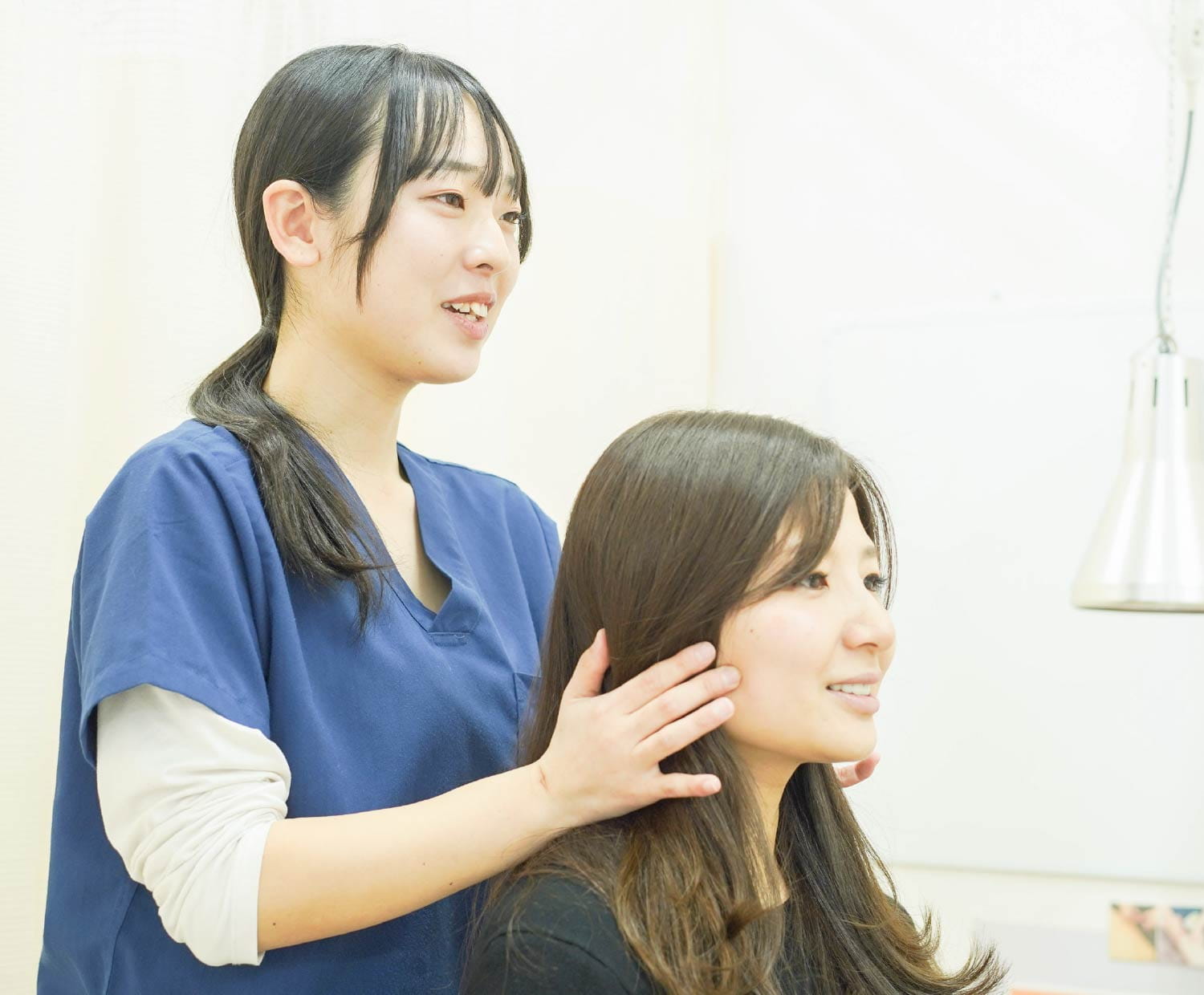 施術着の女性スタッフが、座るお客様の首まわりに手を添えてケアしている様子
