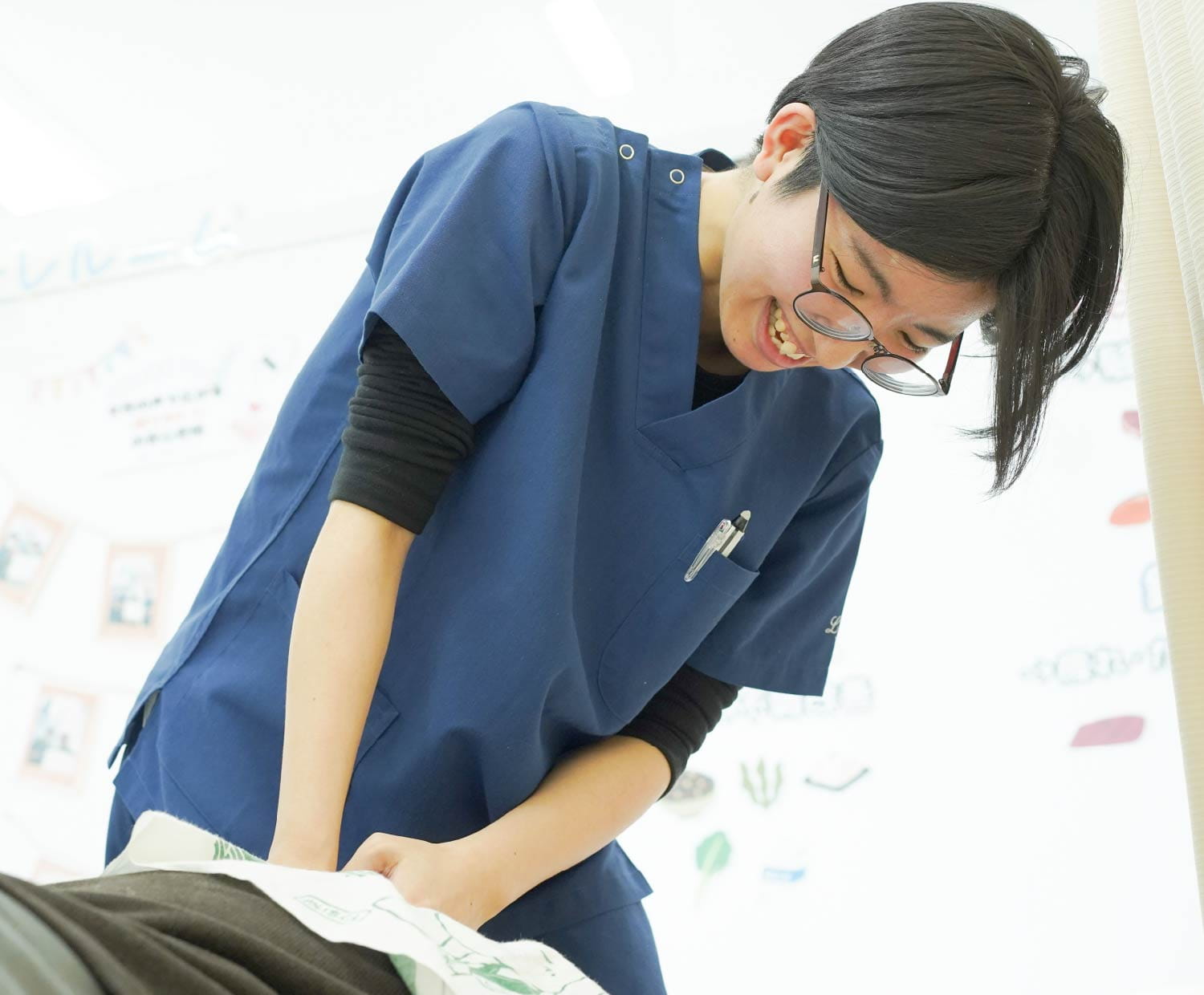 眼鏡の女性施術者が、身を乗り出して施術に集中し穏やかに微笑んでいる様子