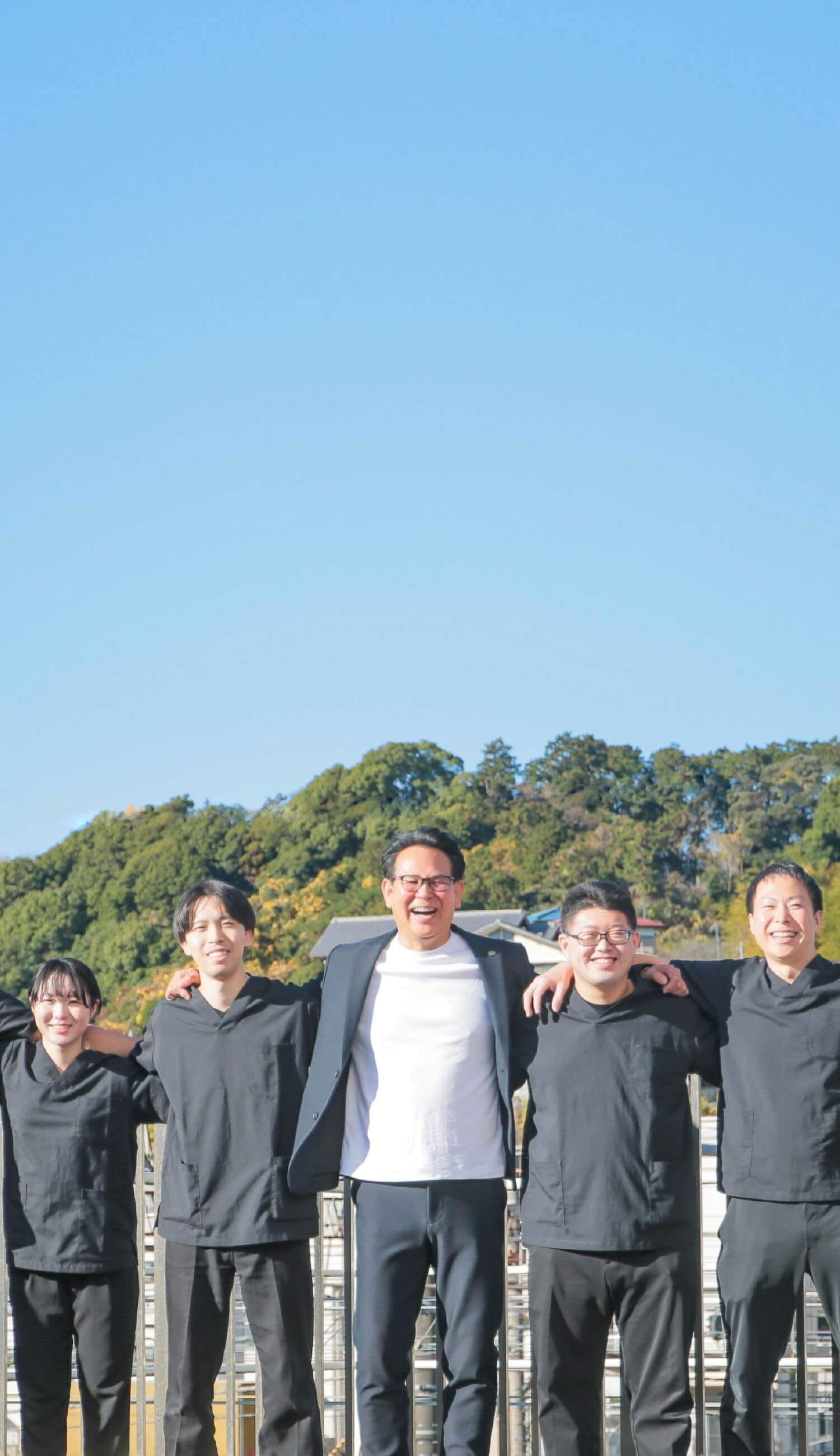大勢の職員が野外で肩を組み笑顔で微笑んでいます