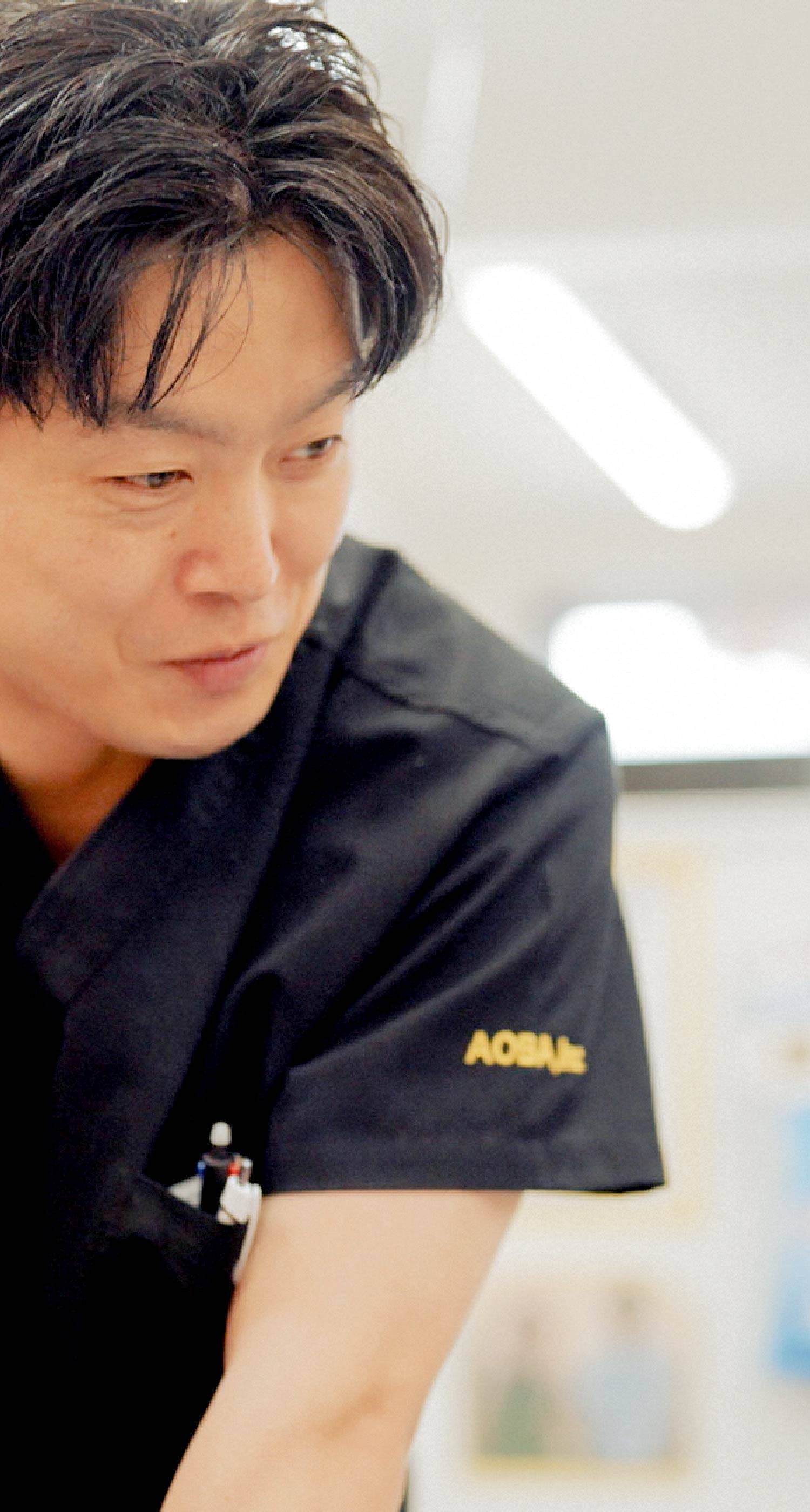 濃紺のスクラブ姿の男性スタッフが、穏やかに微笑んで話しかけている様子