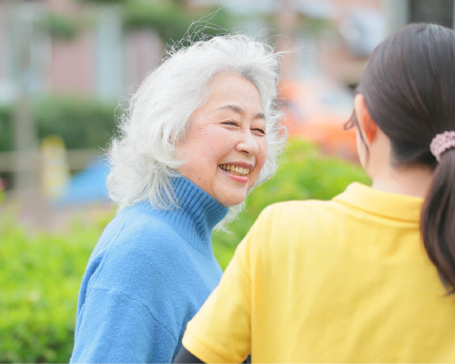 屋外の緑の前で、スタッフと笑顔でのびのびと語らう白髪のご婦人の姿
